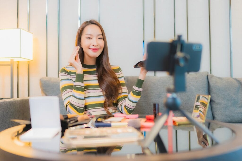 Portrait of a beautiful young Asian woman reviewing and using cosmetics on a sofa