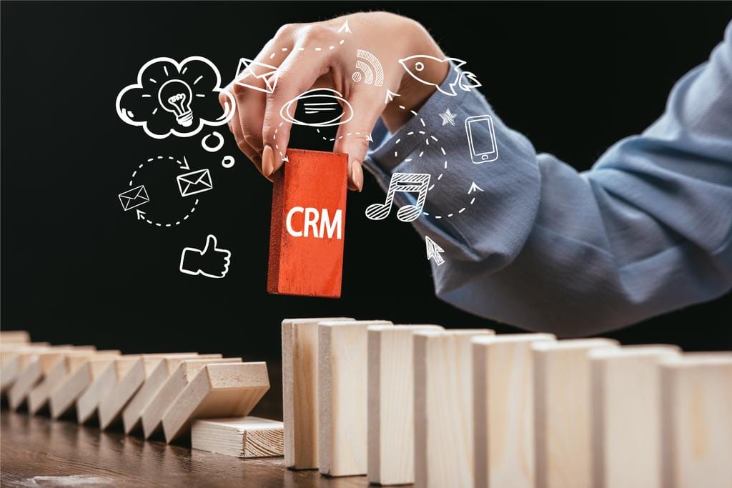 cropped view of woman picking red block word CRM out of wooden blocks